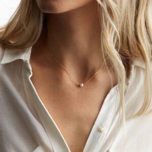 delicate freshwater pearl solitaire necklace worn on neck - blonde woman wearing casual white shirt close-up view