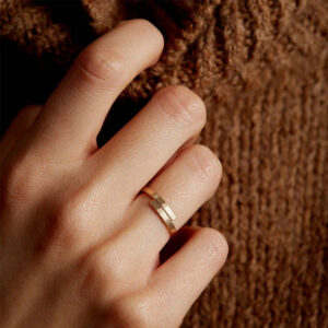 Gold wrap ring worn on hand, showing minimalist thin band design on middle finger against knitted sweater backdrop