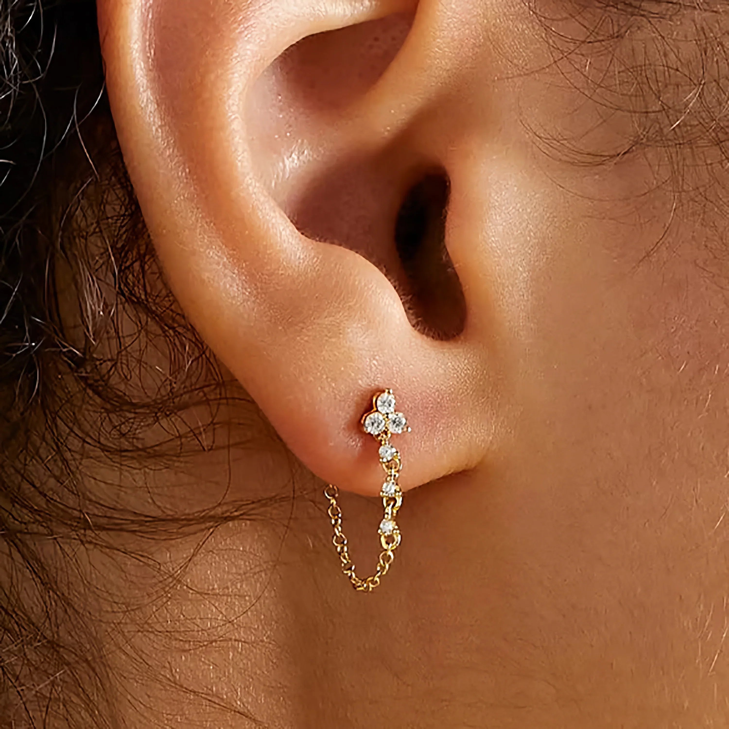 Close-up rear earlobe view of 18K gold chain stud earring with CZ cluster and dangling chain