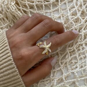 Gold starfish ring worn on model hand with rhinestones on fishing net background close-up