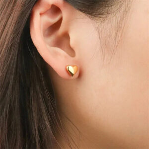 18K gold heart stud earrings worn on ear, close-up side view on female model with long dark hair