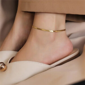 slim 18K gold herringbone anklet worn on female ankle with beige mules close-up side view styling