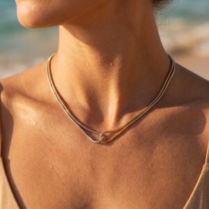 Two-tone 18K gold and silver necklace worn on female model at beach showing interlocked snake chains on neck
