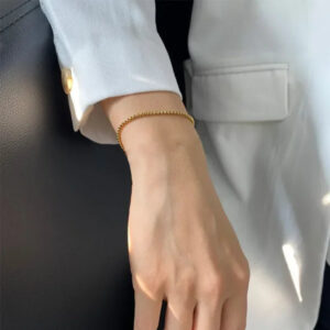 Dainty 18K gold thin box chain bracelet on wrist close-up worn with white blazer minimalist jewelry styling elegant everyday look