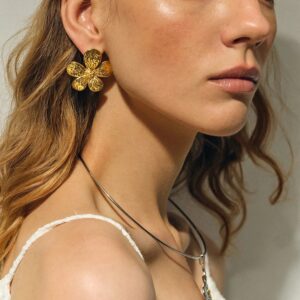 Woman wearing 18K gold daisy flower earrings on earlobe, close-up view showing hammered texture and shine against skin tone