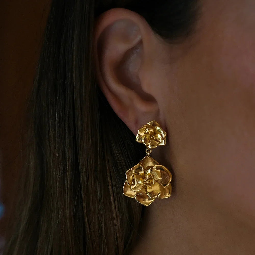 Close-up side view of 18K gold camellia drop earrings highlighting two-tier layered flower petals bright gold plating against dark hair