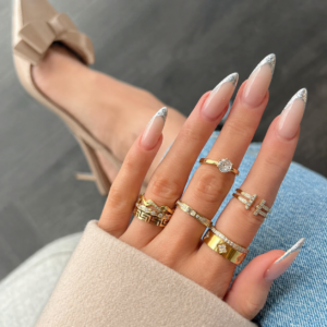 Woman wearing mixed clover and solitaire gold rings on hand with manicure, casual everyday styling