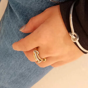 Two-tone 18K gold and silver stackable rings worn on model's hand against blue denim, demonstrating wrapped fit and sleek metal texture in real-world styling