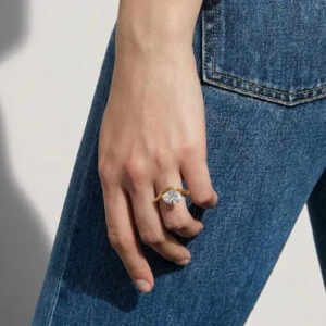 Pear-shaped diamond gold ring worn on finger against blue denim close-up side angle