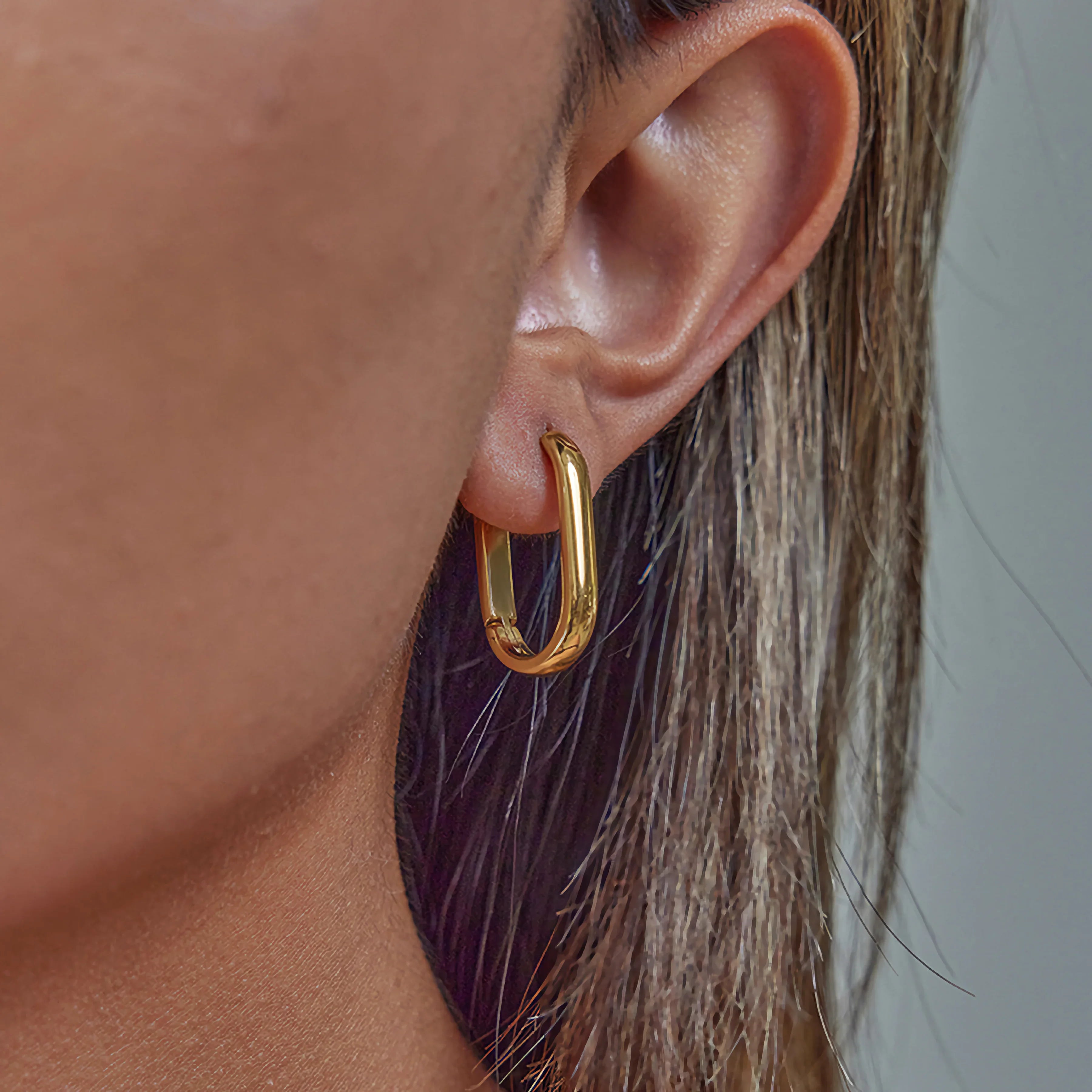 Delicate slim 14mm short gold hoop earrings worn on ear close-up showing minimalist design