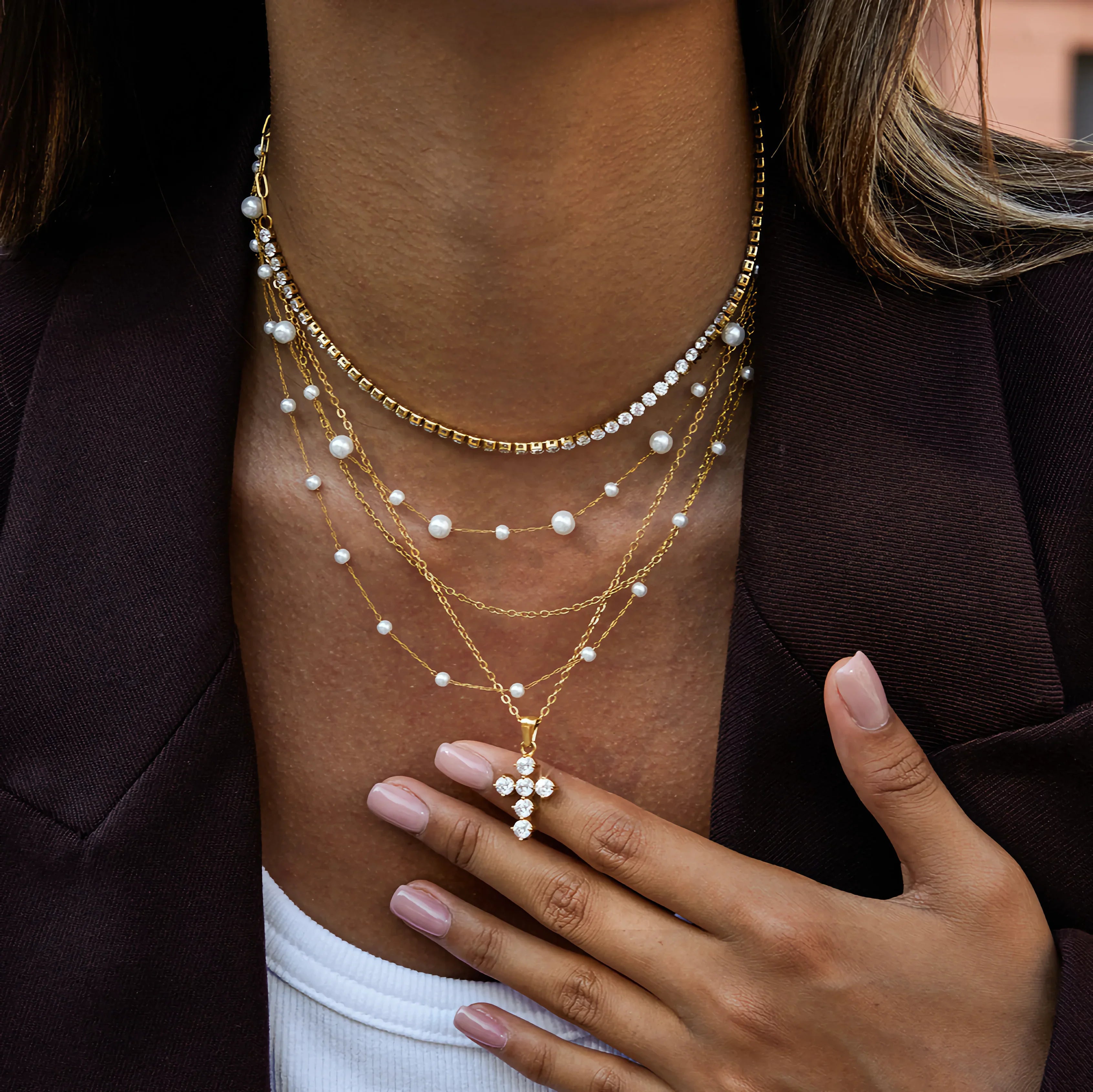 layered 18k gold cross necklace stacked with pearl and delicate chains creating modern multi-strand jewelry look