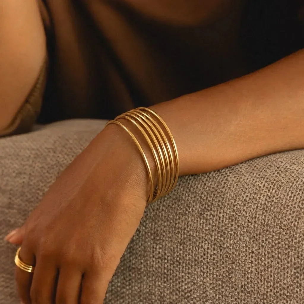 Layered thin gold bangles on woman's wrist - multi-bangle stack styling
