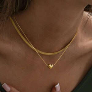 Dual-layer 18K gold necklaces on female model's neck - flat snake chain layered with twisted chain heart pendant