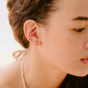14K gold open hoop stud earrings close-up side profile on model with short curly brown hair showing minimalist tiny hoop design on earlobe