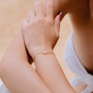 Minimalist freshwater pearl gold bracelet worn on female wrist lifestyle shot sandy background elegant jewelry