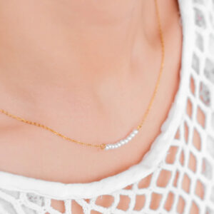 Woman wearing 18K gold curved freshwater pearl necklace on neck, white crochet top, close-up detail view