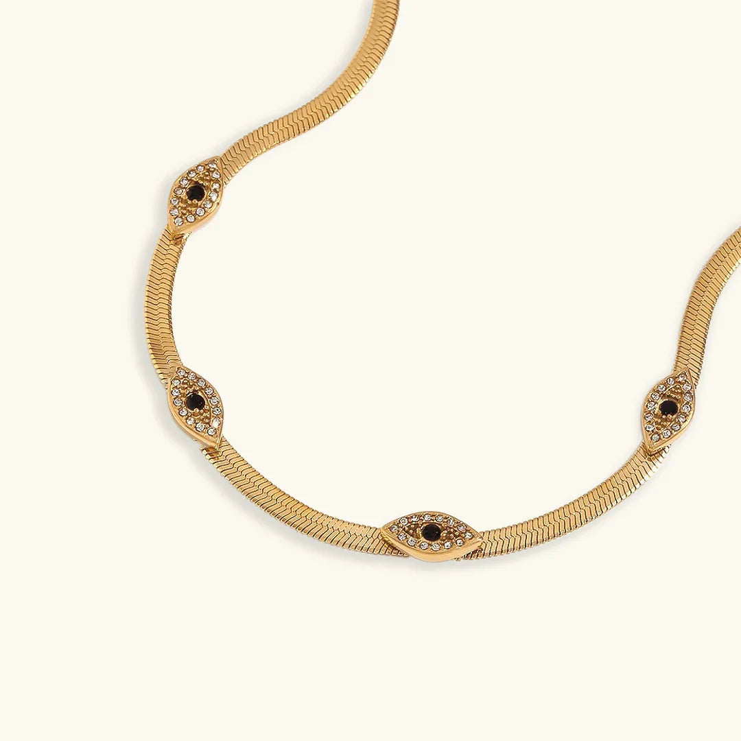 18K gold evil eye herringbone necklace flat lay overhead view featuring gold chain with black enamel and crystal accent evil eye charms