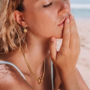 Gold herringbone choker necklace worn on model at beach, side portrait view showing chain drape and matching gold drop earrings