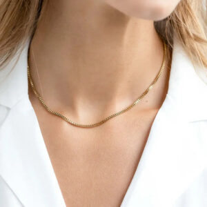Delicate gold box chain necklace worn on female model with white blazer, displaying elegant collarbone fit and minimalist aesthetic