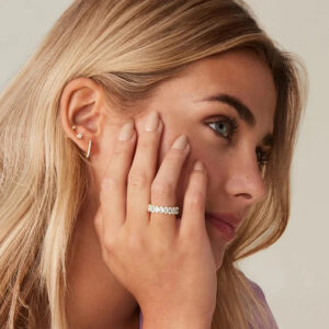 Delicate 18K gold diamond simulant eternity ring worn on model's middle finger, side portrait view
