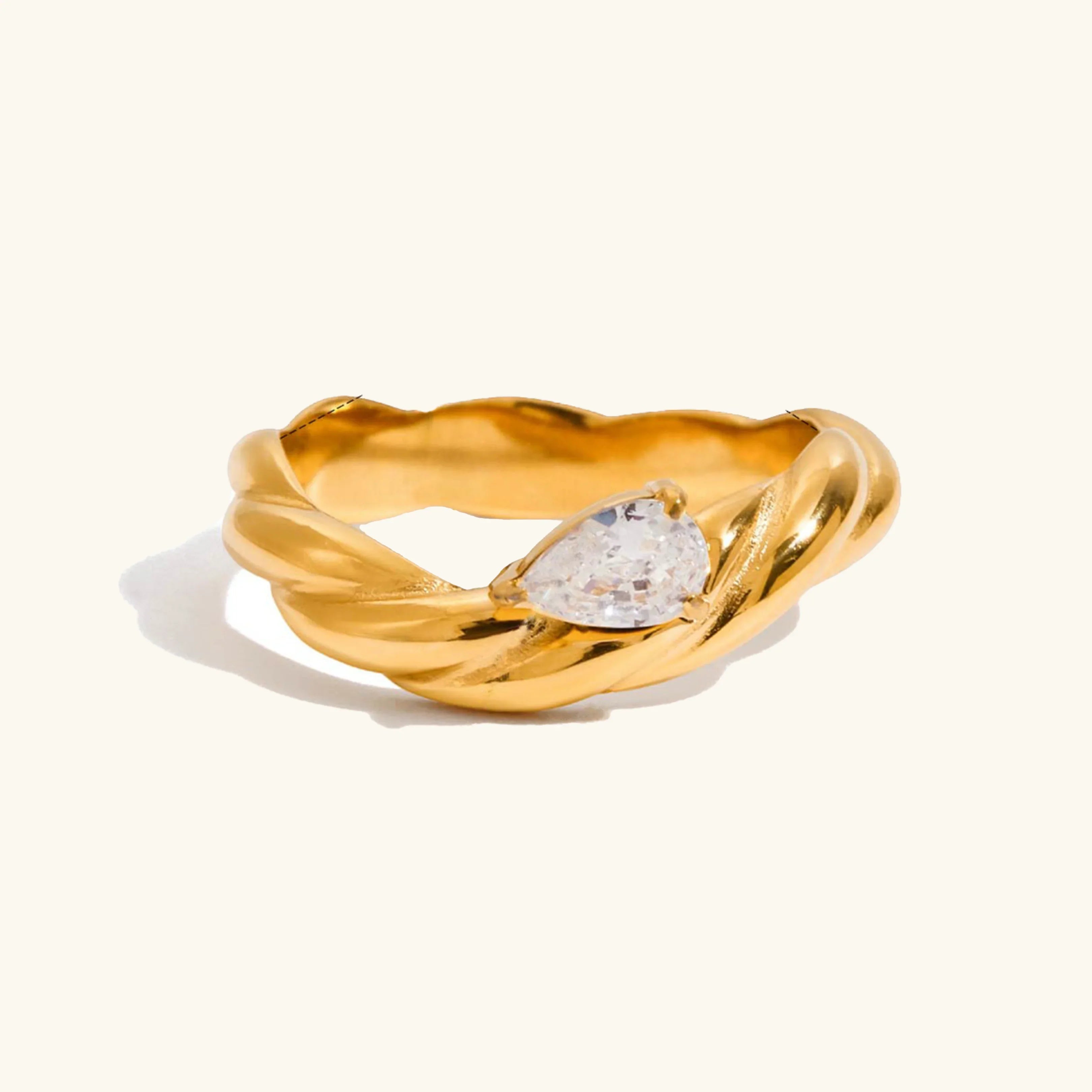 Flat lay studio shot of twisted solitaire 18K gold ring with pear-cut diamond simulant
