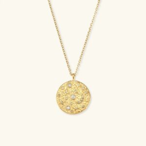 18K gold cosmic disc pendant necklace with hammered texture, pearl and rhinestone centerpiece, displayed on light beige background