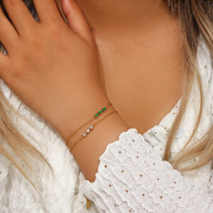 Female model wearing layered 18K gold diamond bracelets with teardrop and pear-shaped gemstones, styled with white ruffled blouse for everyday luxury layered bracelet look
