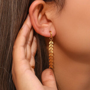 Woman wearing 18K gold fishtail leaf drop earrings close-up side portrait showing tassel pendant hanging from earlobe