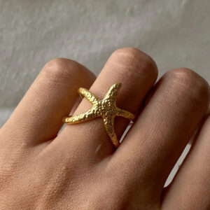 Gold starfish ring worn on finger, close-up detail shot showing polished starfish form and open band on human hand