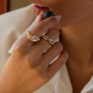 Stacked 18K gold rings on model hand at dining table, teardrop diamond ring with twisted band jewelry