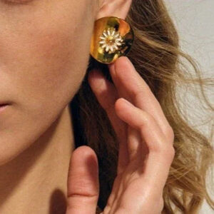 Gold daisy stud earrings worn on ear close-up showing 3D flower detail and curved metal base with side profile of model