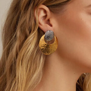 Two-tone crescent earrings worn on earlobe with hammered finish detail close-up on blonde model