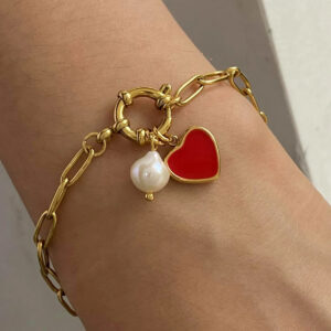 18K gold pearl bracelet worn on woman's wrist - close-up view of heart charm and spring ring clasp in natural light