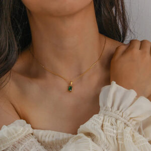 Emerald cut gold necklace worn on woman's neck with off-shoulder ruffled blouse showing slim chain and green stone pendant