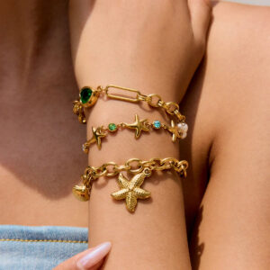 Model wearing stacked 18K gold starfish bracelets on wrist with layered charm details and multi-color gems