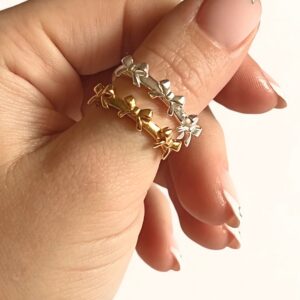Stackable 18K gold and silver bow rings worn on hand with French manicure, close-up side view showing open adjustable band design and bow-shaped decorations