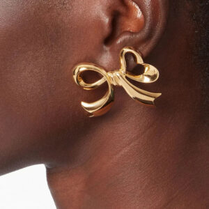 18K gold bow earrings worn on earlobe - close-up profile view showing secure fit and lustrous gold shine on model
