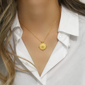 Gold sun coin necklace worn on model with white collared shirt showcasing pendant resting at collarbone on slim gold chain