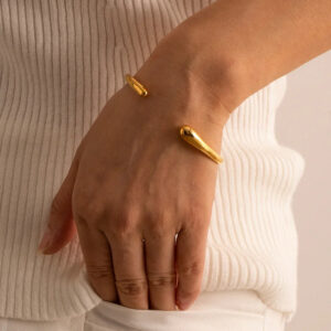 Gold plated open cuff bangle on female wrist close-up teardrop ends shiny tone casual wear