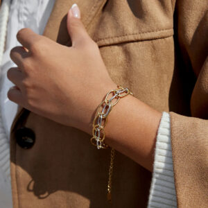 Woman wearing two-tone gold and silver multi-link bracelet on wrist close-up with brown blazer
