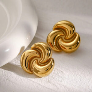 18K gold flower stud earrings three-quarter angle view displaying rounded spiral petal structure and reflective metallic finish on textured linen surface