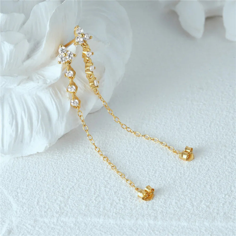 Flat lay 18K gold chain stud drop earrings with dual chains CZ stone accents on textured white background