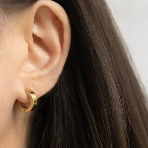 18K gold huggie hoops worn on ear - close-up side view showing sleek fit on earlobe, hypoallergenic gold plated jewelry