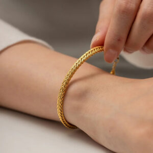 Close-up side view of 18K gold wheat braided bracelet worn on female wrist showing woven chain texture