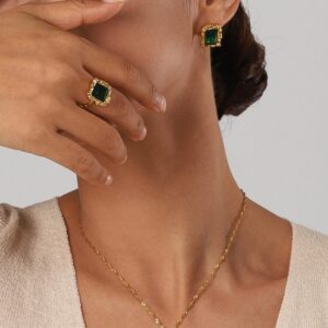 Woman wearing matching emerald jewelry set including emerald ring and stud earrings with necklace elegant styling beige knit top