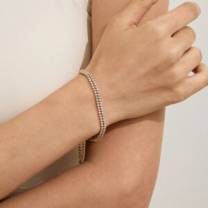 18K gold tennis bracelet worn on female wrist in white activewear, close-up side view showing single-layer pavé crystal design