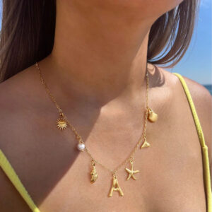 Ocean initial gold charm necklace worn on model at beach close-up detail shot personalized letter pendant yellow camisole