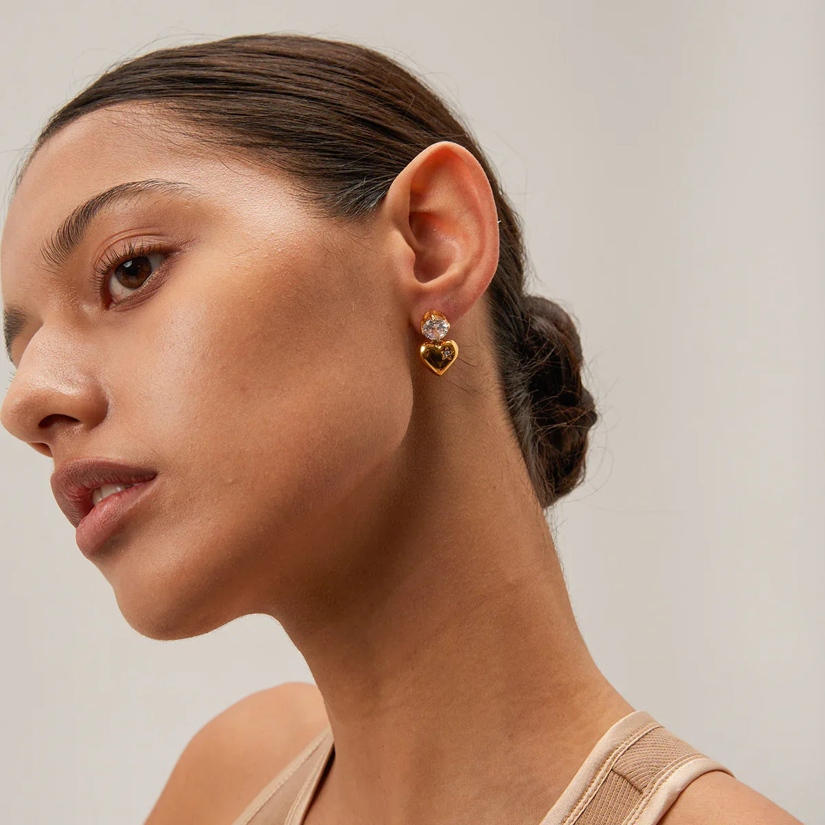 18K gold heart earring worn on ear, side profile close-up detail shot on model with slicked-back hair, showcasing gold heart charm with cubic zirconia accent