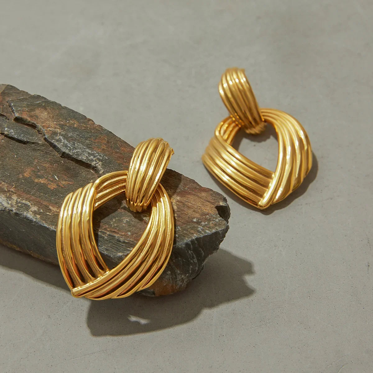 18K gold twisted drop earrings side flat product view rustic stone background geometric loop