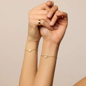 18K gold matching hearts bracelet set worn on wrist - close-up hand view showing thin cable chain, solid heart pendant, and delicate design detail